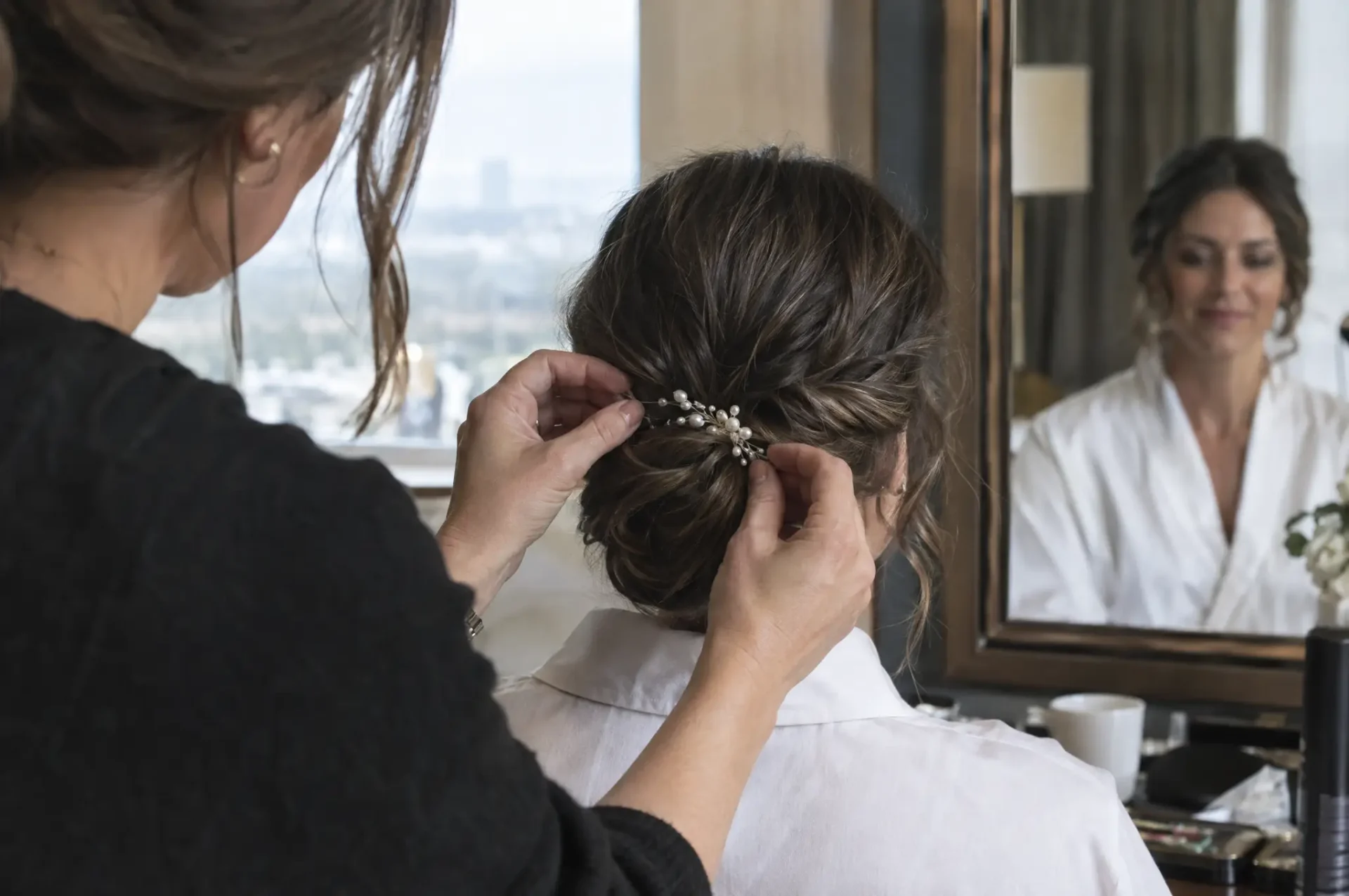 Hairstylist pinning a pearl comb into a bride's low chignon updo